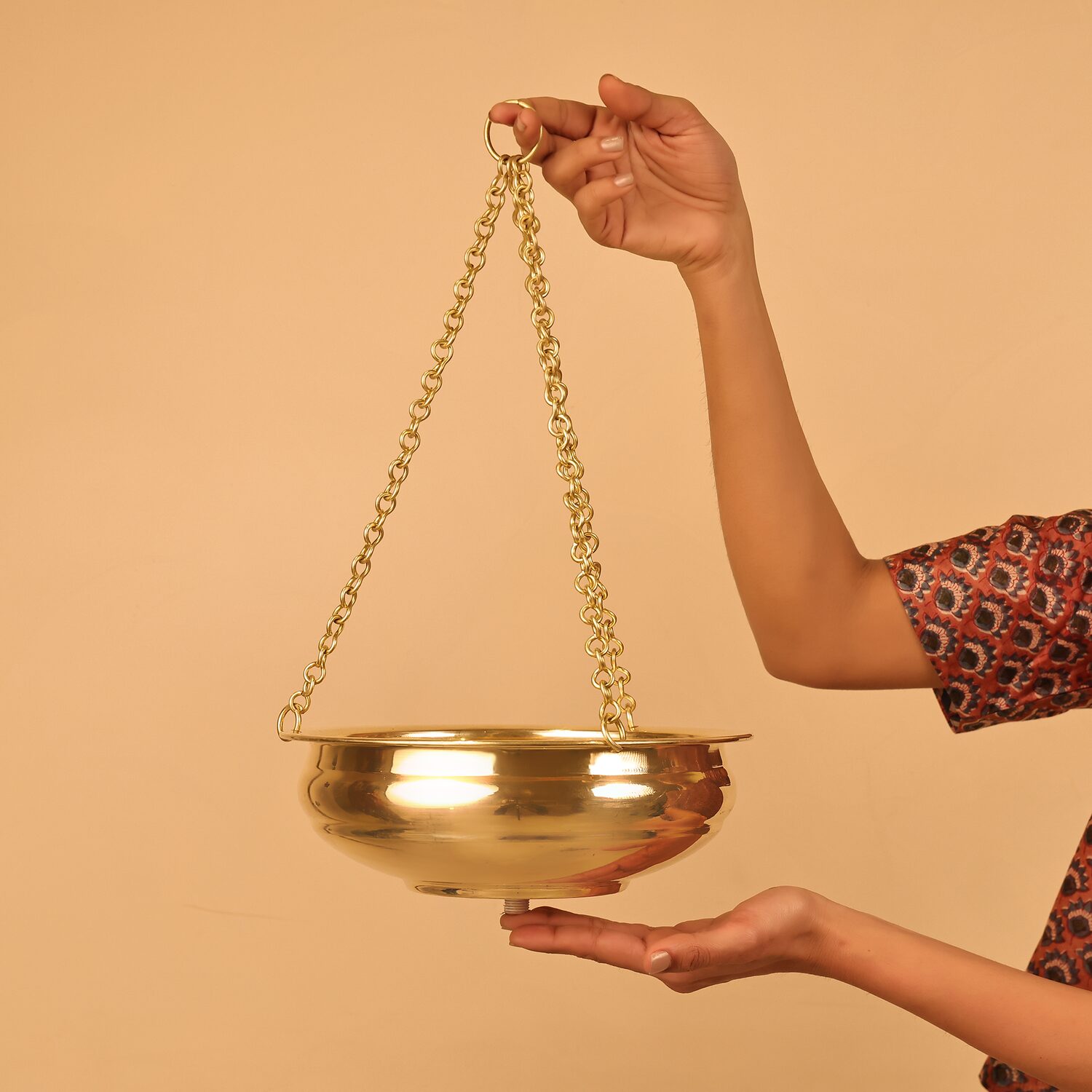 Traditional brass Shirodhara pot with chains and oil-flow valve, held by an Ayurvedic therapist, a Panchakarma instrument for professional Ayurveda treatment rooms